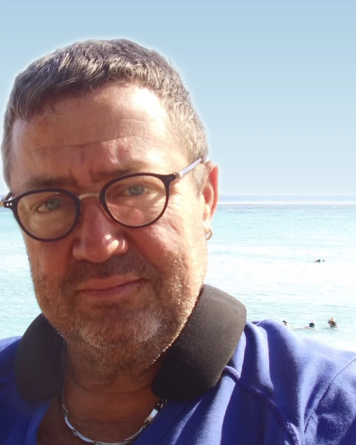 Didier Vitry, gérant de VDIELECT, lunettes rondes et polo bleu, devant le lagon de La Réunion